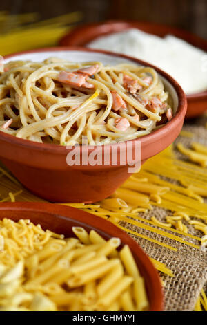 closeup of an earthenware plate with some uncooked pasta, an earthenware bowl with spaghetti alla carbonara, and a bowl with gra Stock Photo