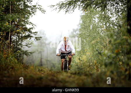 elderly male athlete mountainbiker rides in forest during Regional competitions on cross-country  bicycle Stock Photo
