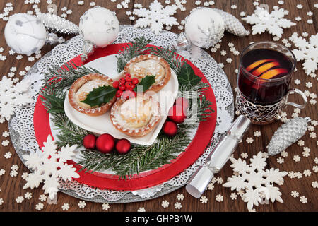 Christmas mince pie cakes with mulled wine, holly, winter greenery, white snowflake and luxury bauble decorations on oak Stock Photo