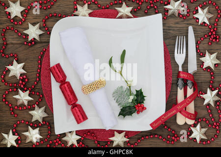 Christmas dinner table setting with white porcelain plate, cracker, napkin,  holly, mistletoe, star bauble and bead decorations, Stock Photo