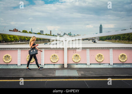 A young woman carrying an expensive handbag crosses The Albert Bridge in Chelsea, London, England, UK Stock Photo