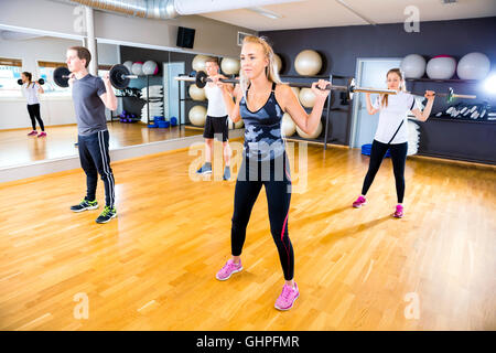 Focused team doing squat exercises with weights at fitness gym Stock Photo