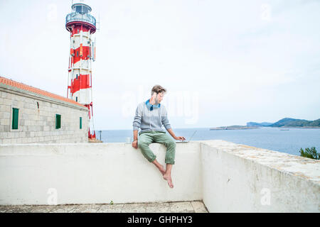 Young man using laptop with lighthouse in background Stock Photo