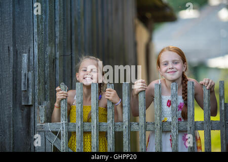 Two little girls having fun posing near a rustic wooden fence. Stock Photo