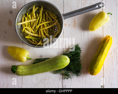 French bean in a colander, zucchini, bell pepper and dill on a white painted wooden surface Stock Photo