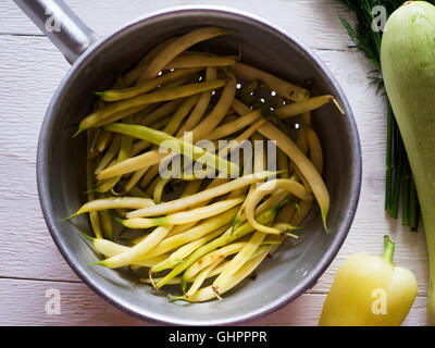 French bean in a colander, zucchini, bell pepper and dill on a white painted wooden surface Stock Photo