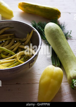 French bean in a colander, zucchini, bell pepper and dill on a white painted wooden surface Stock Photo