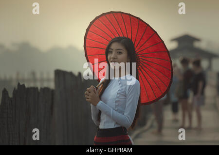 Burmese women in Burmese Traditional dress with red umbrella on U bein bridge Mandalay,Myanmar. Stock Photo