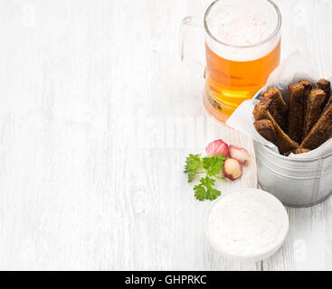 Beer snack set. Pint of pilsener in mug and rye bread croutons with garlic cream cheese sauce over white painted old wooden background, selective focus Stock Photo