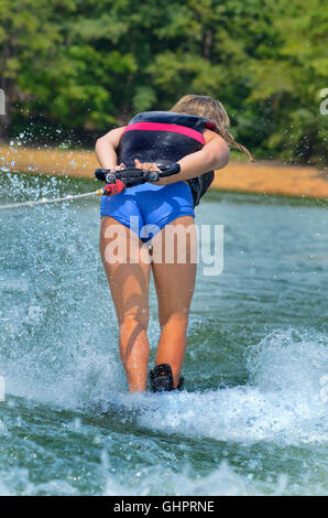 A teenage girl doing tricks on a water ski. She's holding the rope at her back and is turned away from the boat. Stock Photo