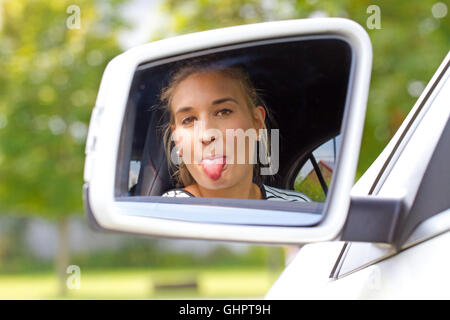 Young woman sticking tongue out in a car mirror Stock Photo