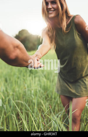 Shot of woman holding hand of her boyfriend and standing in grass field. Loving young couple on meadow outdoors. Stock Photo