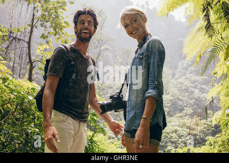 Portrait of happy young couple standing together during rain in the forest. Tourist on hike in forest. Stock Photo