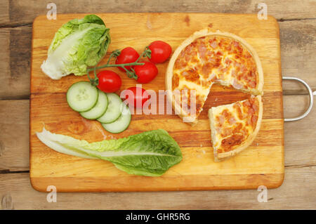 Quiche Lorraine and salad on a wooden board on a rustic wooden tabletop Stock Photo