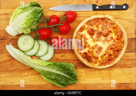 Quiche Lorraine with salad and a kitchen knife on a wooden chopping board Stock Photo