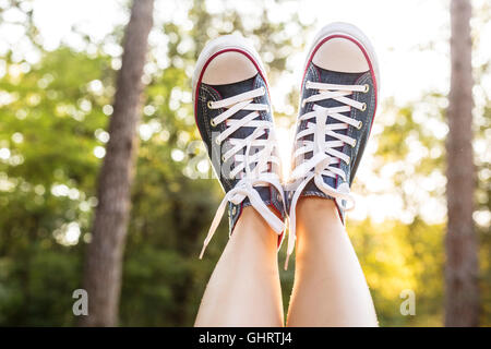 Close view of woman legs  wearing jeans sneakers over a sunset rays in a forest