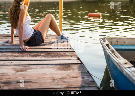 Girl sitting on wooden bench outside in a green park looking at