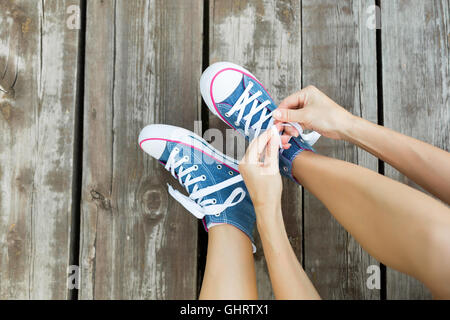 Young woman tying laces of her jeans sneakers sitting on the wooden floor Stock Photo