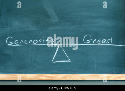 the words generosity and greed on a scale in equilibrium written on a chalkboard. Stock Photo