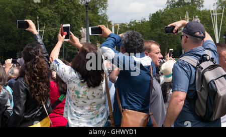 Tourists hold their phones above their heads to take a photo above the crowds at the changing of the guards, London, England Stock Photo