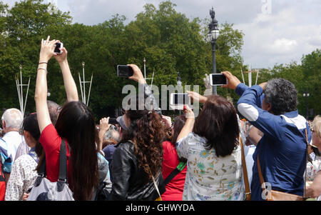 Tourists hold their phones above their heads to take a photo above the crowds at the changing of the guards, London, England Stock Photo