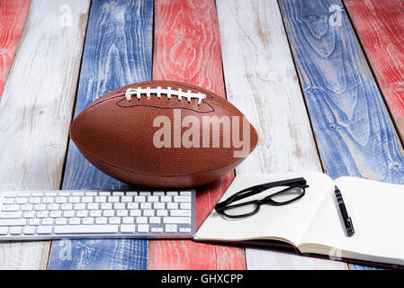 Front view of computer keyboard, reading glasses, notepad, pen and American football on red, white and blue rustic wooden boards Stock Photo