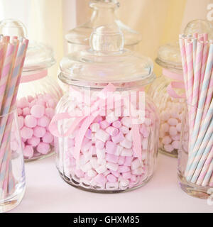 Square view of jars of pink sweets and old fashioned paper straws.