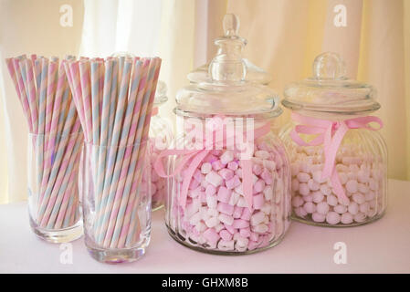Horizontal view of jars of pink sweets and old fashioned paper straws.