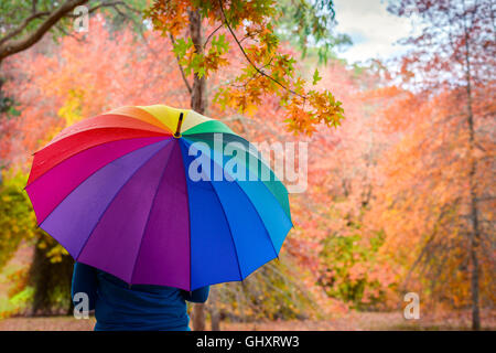 Woman standing under rain in autumn park with colorful umbrella Stock Photo