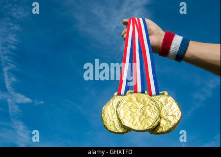 Hand of American athlete holding gold medals hanging from USA colors red, white, and blue ribbon against a bright blue sky Stock Photo