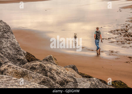 A young man walking his dog on Cattersty Sands at Skinningrove,North Yorkshire Stock Photo