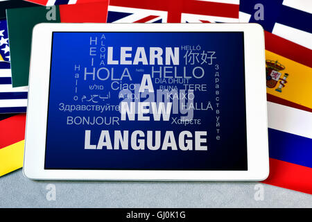the text learn a new language and the word hello in different languages in the screen of a tablet computer, surrounded by flags Stock Photo