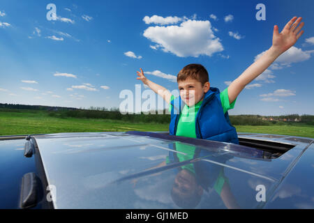 Smiling kid boy enjoying freedom on sunroof of car Stock Photo