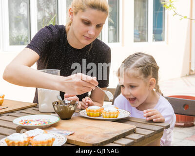 Mom puts confectionery glaze spoon on Easter cupcake, daughter happily looking Stock Photo