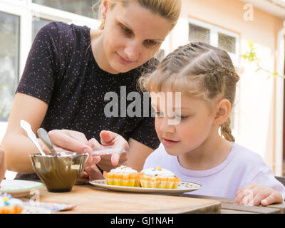 Mother pours a bag of confectionery posypku on Easter cupcake, daughter happily looking Stock Photo