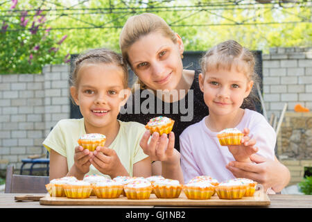 Mother and two daughters sitting at the table with Easter cupcakes in his hands and looked into the frame Stock Photo