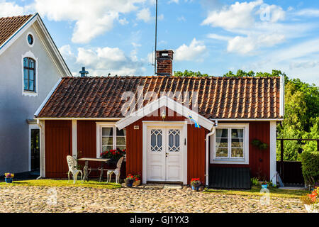 Pataholm, Sweden - August 9, 2016: Small red wooden house by the village square in the evening. Outdoor furniture in front of bu Stock Photo