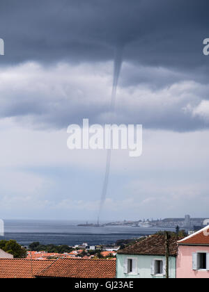 Waterspout over Ponta Delgada. A tornadic waterspout appears from the dark storm clouds in the ocean just beyond the city centre Stock Photo