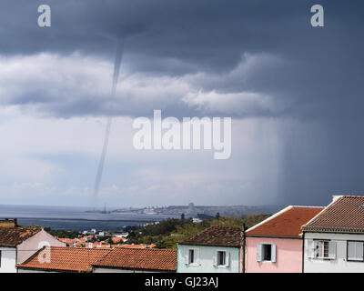 Waterspout over Ponta Delgada. A tornadic waterspout appears from the dark storm clouds in the ocean just beyond the city centre Stock Photo