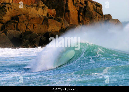 A crisp blue wave crashes against a granite cliff Stock Photo
