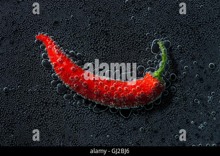 Chili pepper in a mineral water, a series of photos. Close-up carbonated water against black background Stock Photo