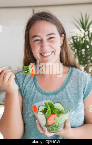 Teenage girl holding bowl of salad looking at camera smiling Stock Photo
