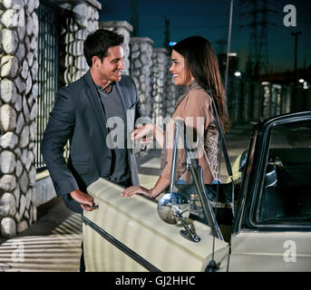 Man helping woman out of classic car at night, Los Angeles, California, USA Stock Photo