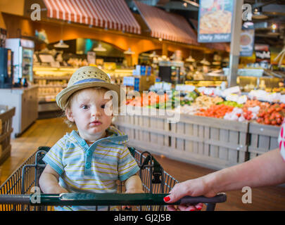 Baby boy wearing straw hat sitting in shopping trolley Stock Photo