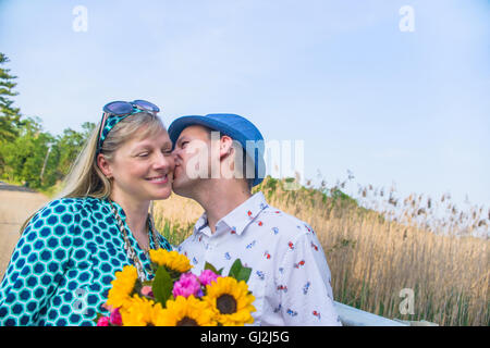 Couple holding flowers, kissing on cheek Stock Photo
