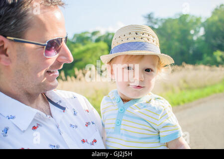 Father holding baby boy wearing straw hat Stock Photo