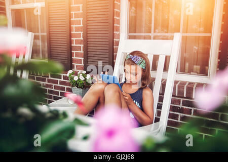 Girls on porch in rocking chair using digital tablet Stock Photo