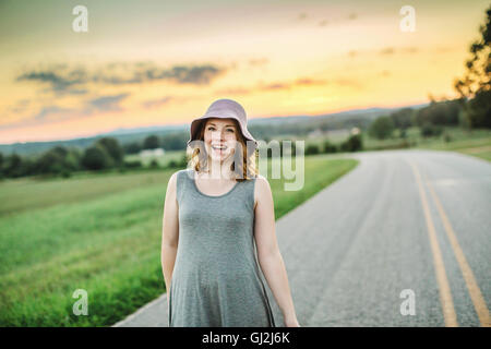 Woman on rural road wearing sunhat looking at camera smiling Stock Photo
