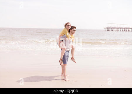 Man on beach giving woman piggyback, Coney island, Brooklyn, New York, USA Stock Photo