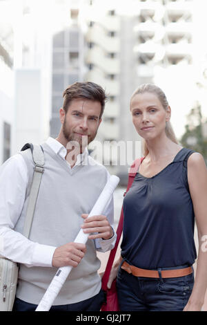 Portrait of man and woman outdoors, man holding rolled up documents Stock Photo